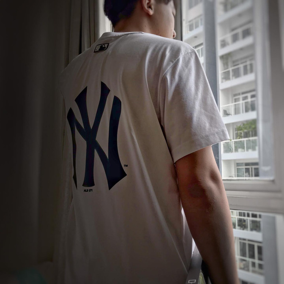 a person wearing a New York Yankees t-shirt standing in front of a window